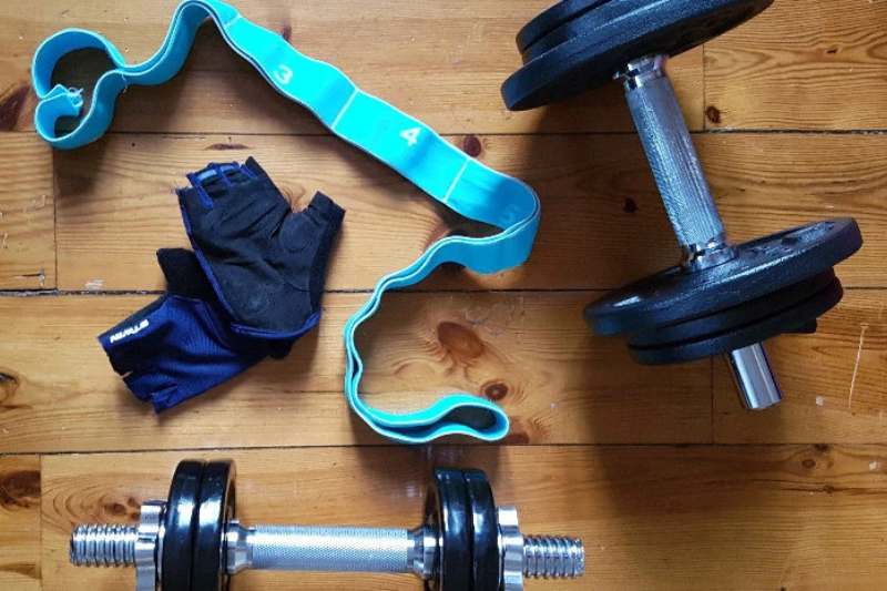 Exemple d’accessoires et équipements de sport à domicile, une niche en pleine croissance dans le secteur de l’e-commerce en Tunisie : haltères réglables, gants de musculation et bandes élastiques de résistance sur un sol en bois.